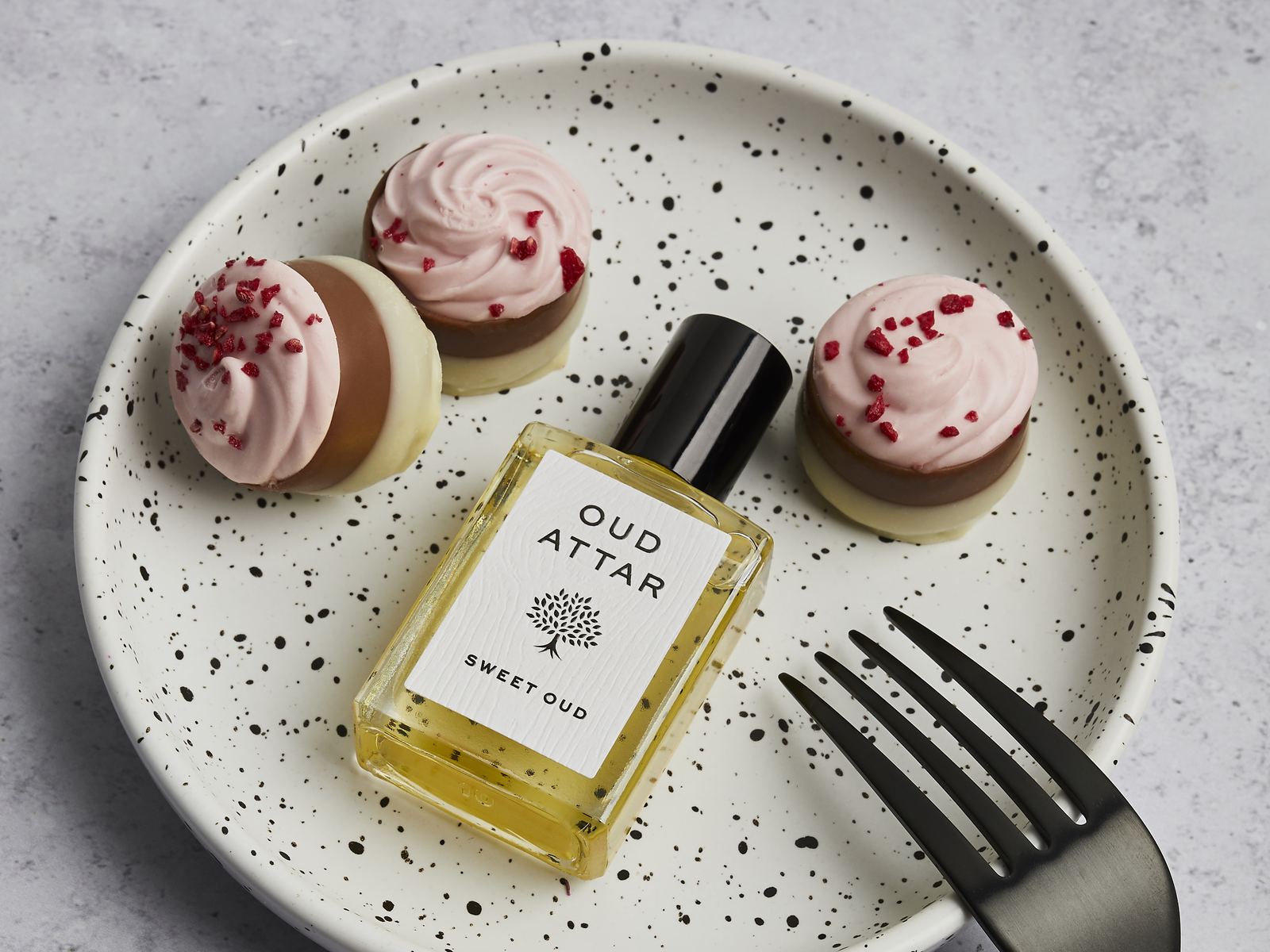 Sweet Oud perfume oil on a speckled plate with iced cakes and a fork