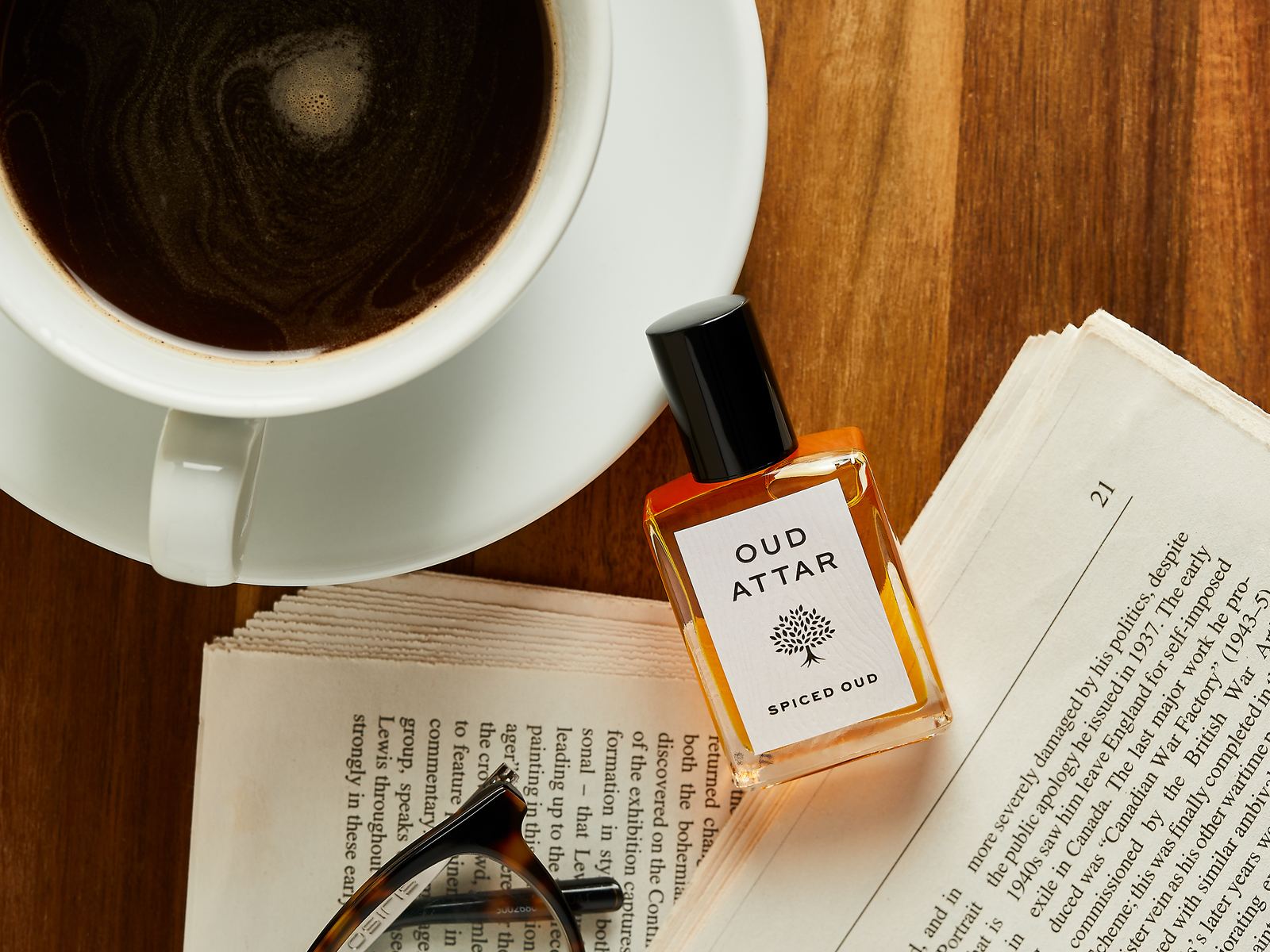 Spiced Oud perfume oil on an open book beside a cup of coffee and reading glasses