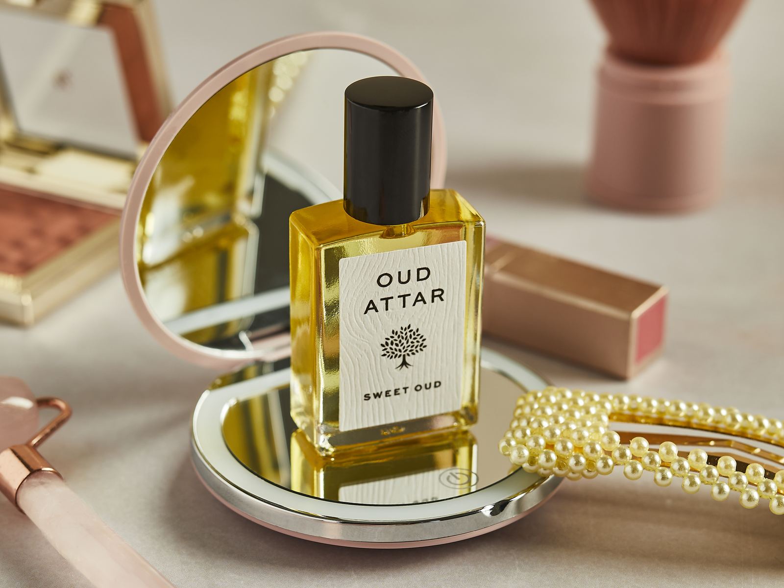 Sweet Oud perfume oil on a dressing table with a mirror, pearls and a make-up brush