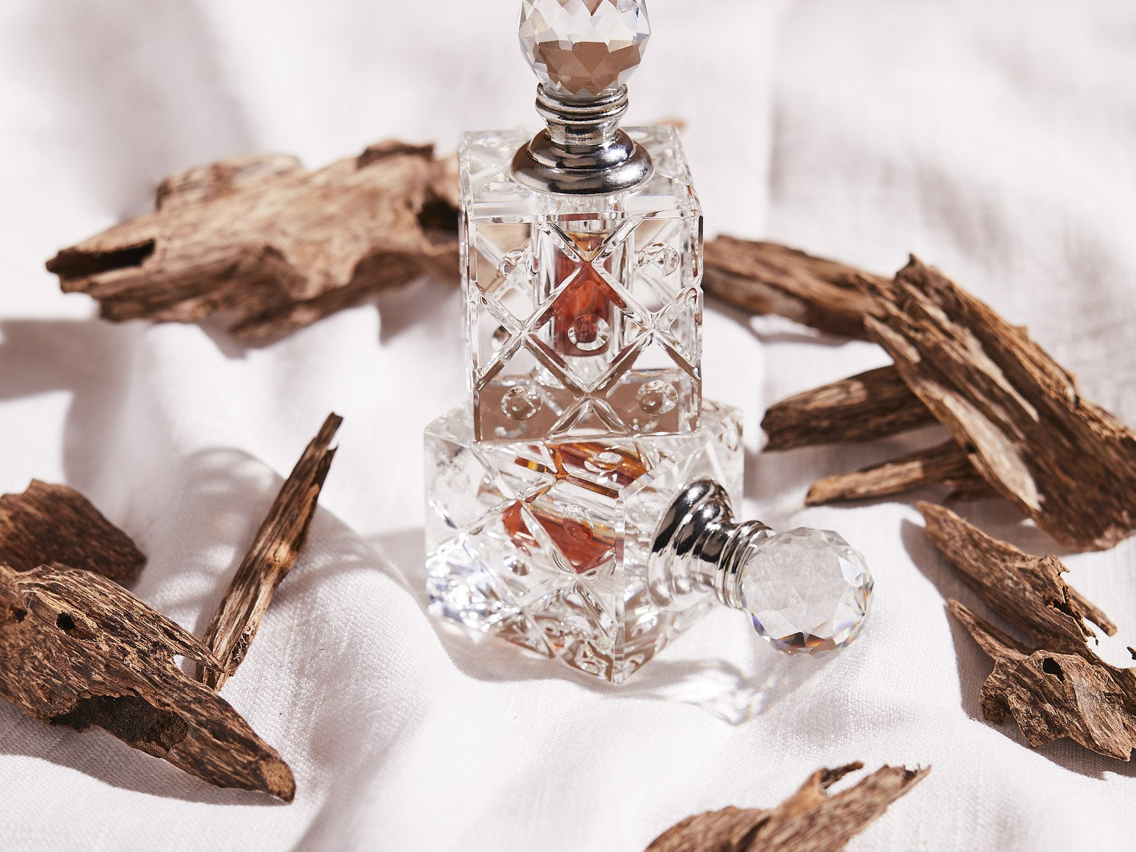 Crystal bottle of pure oud oil among agarwood chips on white linen